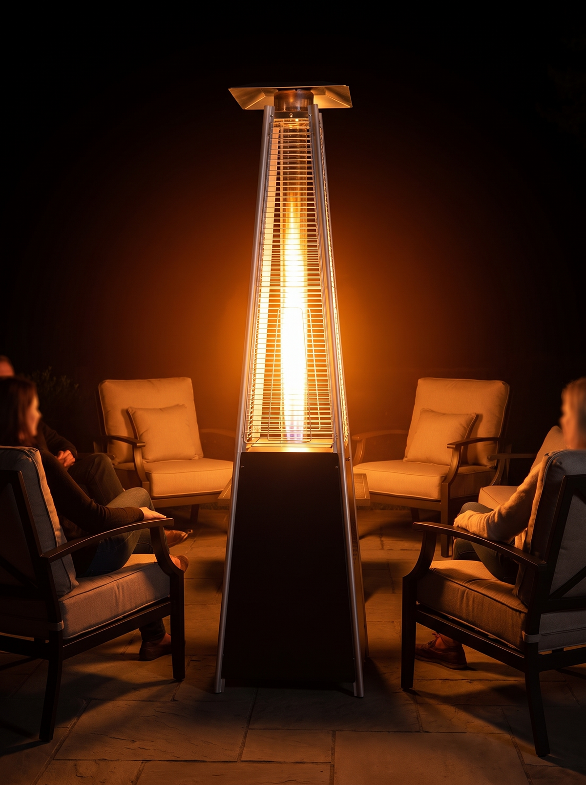Pyramid propane patio heater lit at night radiating 360 degree warmth around seating